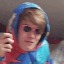 a man wearing a blue hoodie and pink sunglasses is holding a red remote control .