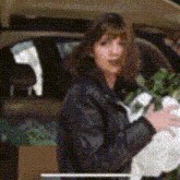 a woman in a black jacket is standing in the back of a car holding a bouquet of flowers