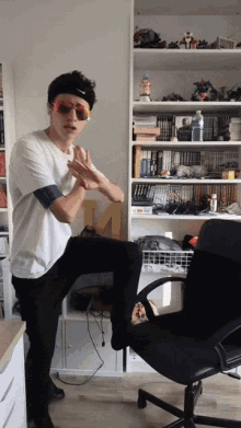 a man wearing sunglasses and a nike headband stands in front of a bookshelf
