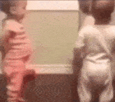 two babies are standing next to each other in a room