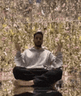 a man is sitting in a lotus position with his feet crossed in front of a wall of flowers .