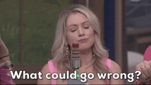 a woman in a pink tank top is holding a microphone and asking what could go wrong .