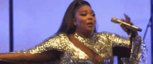 a woman in a silver dress is singing into a microphone on stage .