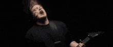 a man in a black shirt is playing a guitar with his mouth open