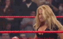 a blonde woman is standing in a wrestling ring with a crowd behind her .