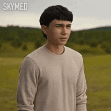 a young man in a white sweater is standing in a field with the words skymed behind him