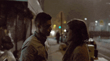 a man and a woman are looking at each other on a sidewalk at night