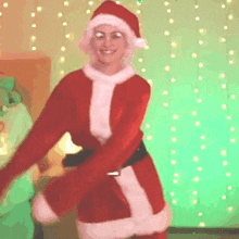 a woman in a santa suit is dancing in front of a green background .
