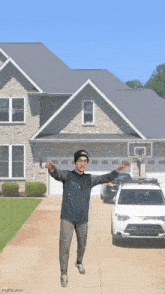 a man standing in front of a house with his arms outstretched and a car parked in front of him