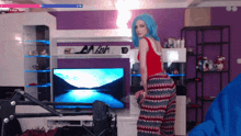 a woman with blue hair is standing in front of a television with a purple wall