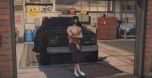 a shirtless man stands in front of a truck in a garage with a smiley face on the wall