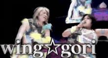 two women are standing next to each other in front of a sign that says " wing gori "