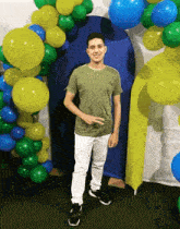 a young man in a green shirt stands in front of a bunch of balloons