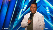 a man in a white jacket is holding a microphone in front of a blue background that says nbc on it