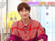 a young man wearing a plaid shirt and a purple jacket is smiling