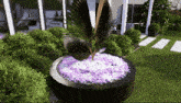 a statue of a bird with purple flowers in a black planter