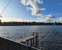 a large body of water with a dock in the foreground and a blue sky with clouds in the background