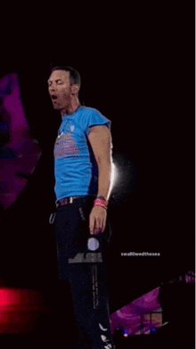 a man in a blue shirt is singing into a microphone on stage