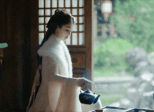 a woman in a white coat is pouring tea into a black teapot