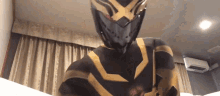 a person in a black and gold superhero costume is standing in front of a window .