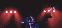 a man is singing into a microphone on a stage with red lights behind him