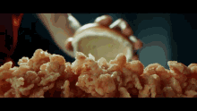 a person holding a slice of lemon over a pile of fried chicken