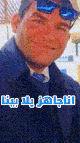 a man wearing sunglasses and a black coat is smiling with arabic writing on the bottom