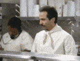 a man in a white shirt and tie is standing in a kitchen next to a woman .