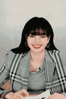 a woman wearing a plaid jacket and a sweater is smiling while sitting at a table .