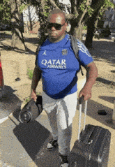a man wearing a qatar airways shirt is carrying a suitcase