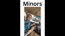a man in a blue plaid shirt is sitting in a car with the word minors on the bottom right