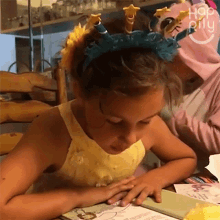 a little girl wearing a headband with stars on it is sitting at a table reading a book .
