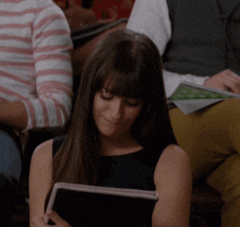a woman in a black dress is sitting in a classroom holding a tablet