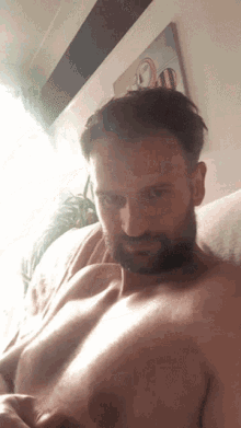 a shirtless man with a beard is sitting on a bed