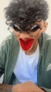 a young man with curly hair and glasses is wearing fake lipstick on his face .