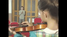 a girl is playing a violin in front of a mirror while a boy is standing behind her .