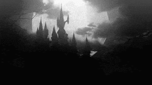 a black and white photo of a castle surrounded by trees and clouds