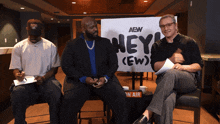 three men sit in front of a sign that says aew hey