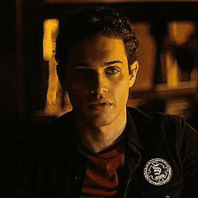 a young man wearing a black jacket and a red shirt is sitting in front of a bookshelf .