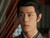 a close up of a man 's face in a room with a red curtain behind him .
