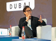 a man speaking into a microphone with a dubai sign behind him