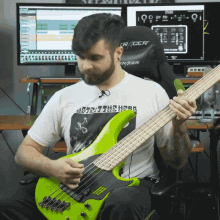 a man is playing a green bass guitar and wearing a shirt that says lost in the hood