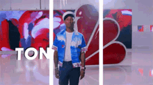 a man in a blue shirt is standing in front of a wall with the word ton written on it