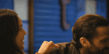 a man and a woman are sitting at a table and the woman is pointing at the man 's face .