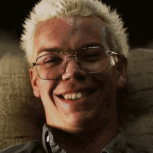 a man with blonde hair wearing glasses is smiling
