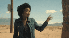 a woman in a blue jacket stands in the desert