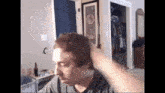 a man is brushing his hair in a room with a picture on the wall .