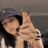 a woman with long black nails is wearing a hat