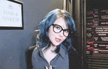 a woman with blue hair and glasses stands in front of a sign that says hair and makeup