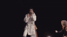 a man in a white robe is singing into a microphone in the dark